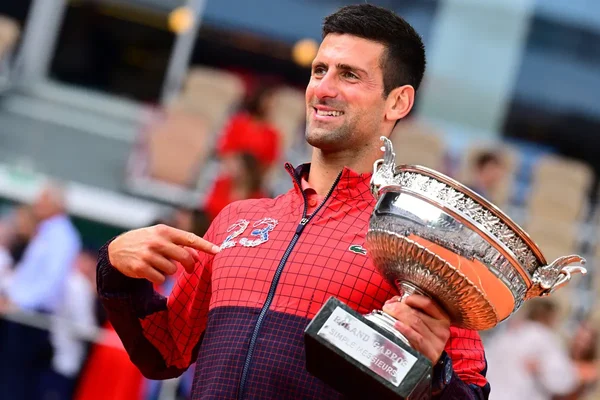 Novak Djokovic avec son 23e titre du Grand Chelem, souriant et pointant le chiffre brodé.
