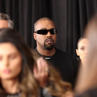 Kanye West, lunettes noires et chemise sombre, devant un rideau noir.