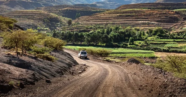 SUV blanc sur une route de terre sinueuse dans un paysage agricole en Éthiopie.
