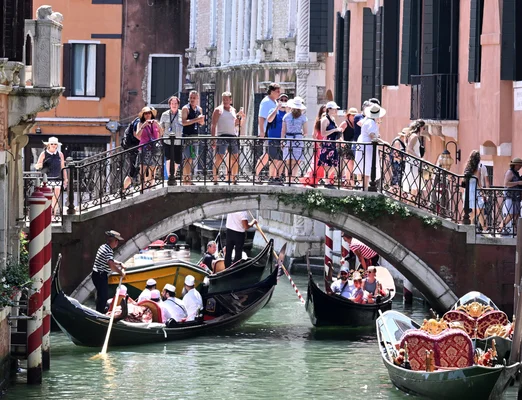 Gondoles et touristes sur un canal de Venise, sous un pont bondé.