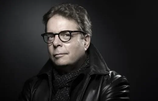 Portrait noir et blanc de Douglas Kennedy, veste en cuir et écharpe, regard déterminé.