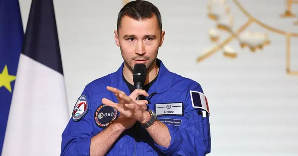 Arnaud Prost, astronaute français, en combinaison spatiale devant un drapeau tricolore.