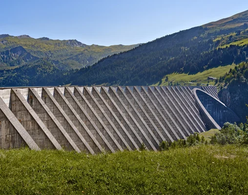 Barrage voûte en béton avec contreforts, dans un paysage de montagne verdoyant.
