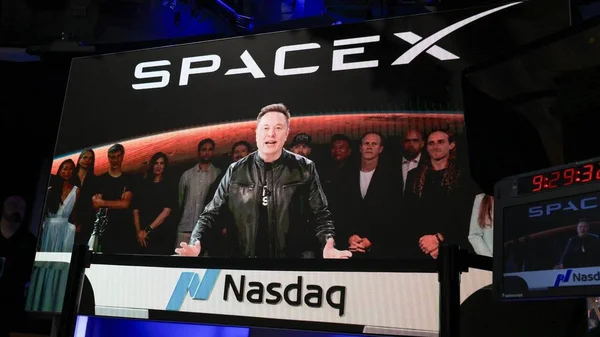 Elon Musk s'adressant à un public lors d'un événement au Nasdaq, avec le logo SpaceX visible.