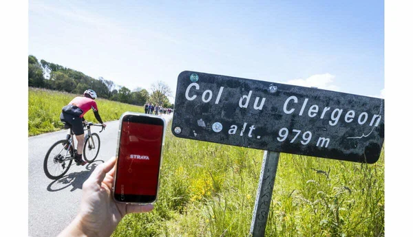 Cycliste gravissant le Col du Clergeon avec un smartphone affichant Strava au premier plan.