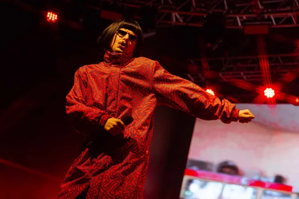 Oliver Tree lors d'une performance sur scène, reconnaissable à sa perruque noire et ses lunettes de soleil.