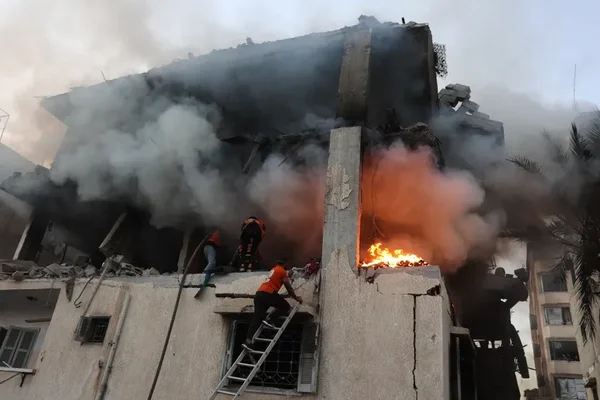 Un bâtiment en feu à Gaza après des frappes israéliennes, avec des secouristes sur place.
