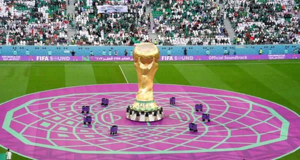 Réplique géante du trophée de la Coupe du Monde sur la pelouse d'un stade bondé.