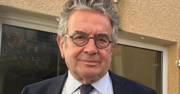 Alain Claeys debout devant un bâtiment, en costume sombre.