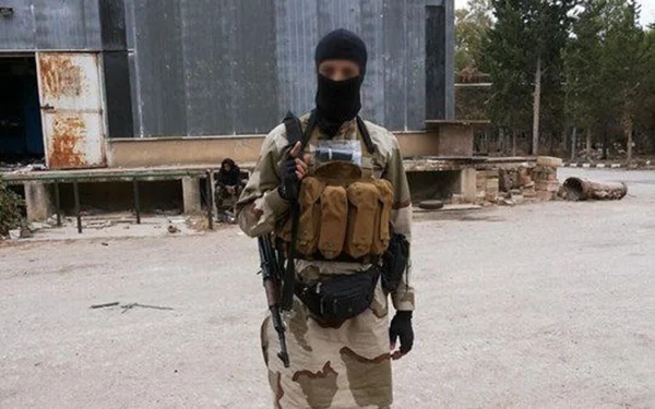 Homme armé en tenue de camouflage et cagoule, lié au recrutement djihadiste pour la Syrie.
