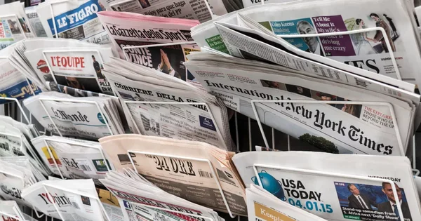 Présentoir de journaux internationaux dans un kiosque, en arrière-plan de la grève au Monde.