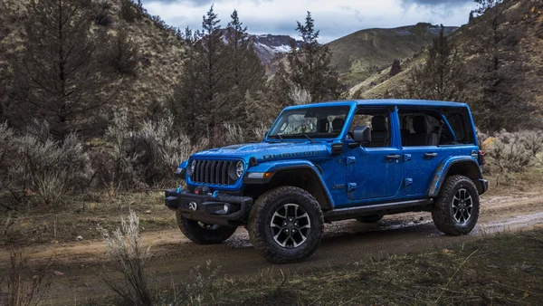 Un Jeep Wrangler Rubicon bleu circulant sur un chemin boueux en montagne, sous un ciel dégagé.
