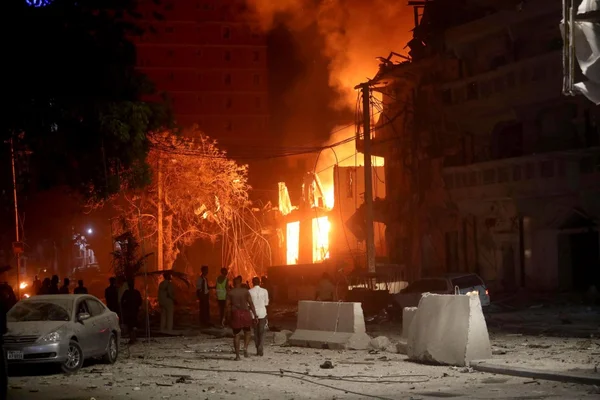 Un bâtiment en flammes à Mogadiscio, avec des badauds et secouristes dans la rue.