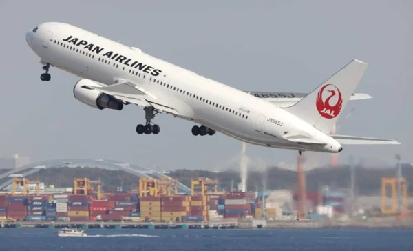 Un Boeing 767 de Japan Airlines décollant au-dessus d'un port industriel.