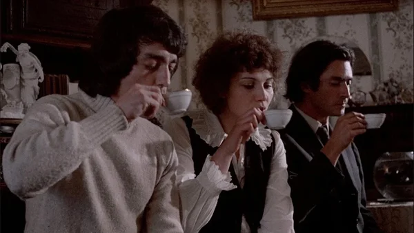 Scène du film « Happy Birthday » montrant trois personnages attablés dans un intérieur rétro.