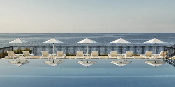 Chaises longues et parasols blancs au bord d'une piscine à débordement sur la Côte d'Azur.