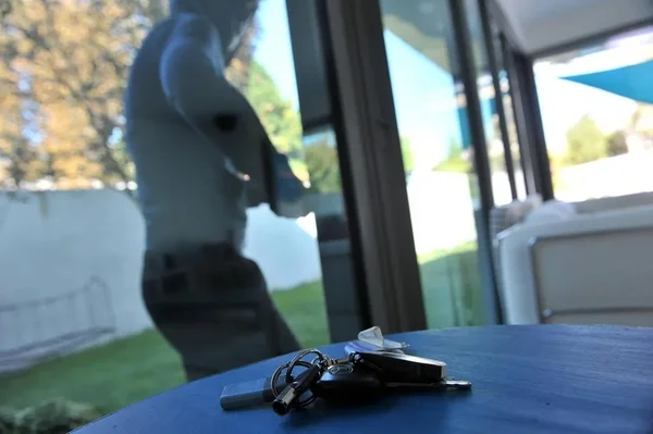 Des clés sur une table, avec une silhouette floue derrière une porte vitrée, évoquant la menace d'un home-jacking.