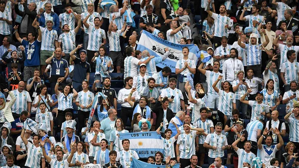 Des supporters argentins en maillots rayés bleu et blanc célébrant dans les tribunes d'un stade.