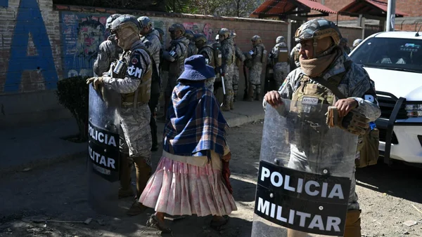 Des policiers militaires gardent une rue tandis qu'une femme âgée en tenue traditionnelle passe.