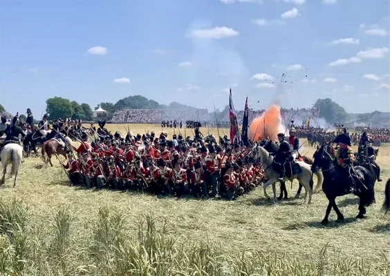Soldats en uniformes rouges en formation carrée lors de la reconstitution de Waterloo, avec cavalerie et fumée.