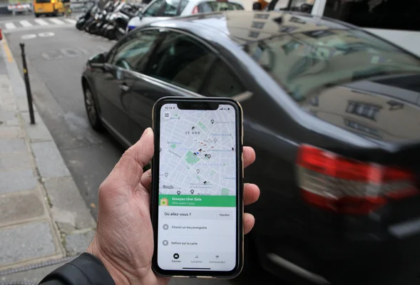 Application Uber affichée sur un smartphone devant une voiture noire dans une rue parisienne.