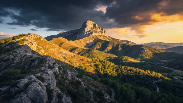 Vue large du Pech de Bugarach, montagne au sommet arrondi dominant les collines des Corbières, ciel dramatique avec nuages sombres, lumière dorée du coucher de soleil