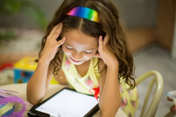 Enfant souriante utilisant une tablette, illustrant l'importance des outils de protection parentale.