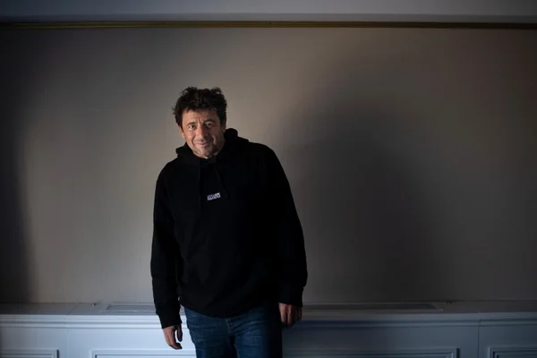 Patrick Bruel, tenue décontractée, fond neutre.