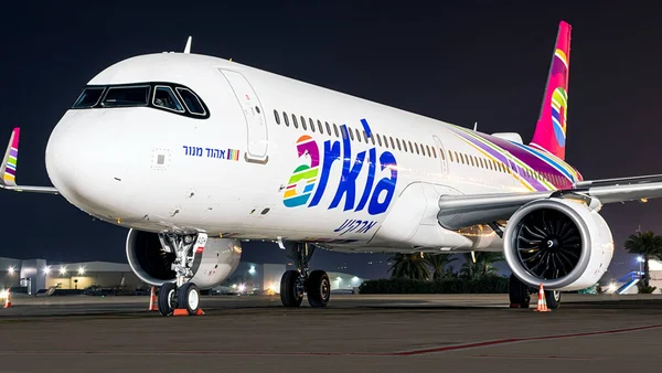 Un Airbus A320neo d'Arkia stationné sur le tarmac d'un aéroport de nuit, éclairé par des projecteurs.