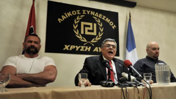 Conférence de presse des dirigeants d'Aube Dorée avec leur emblème et le drapeau grec.