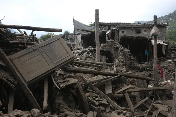 Décombres d'un séisme en Afghanistan : structures en pierre et en boue effondrées, avec une porte en bois penchée contre les ruines.