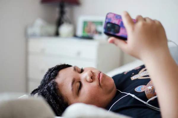 Adolescente utilisant son smartphone et des écouteurs, illustrant les usages numériques des jeunes.