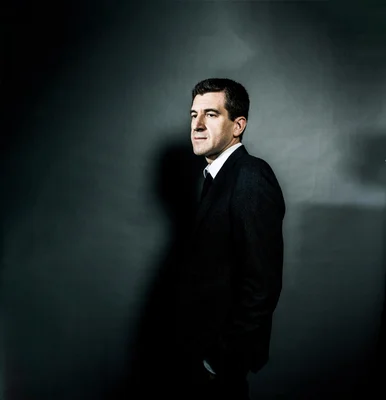 Matthieu Pigasse de profil, en costume noir, sur fond gris.