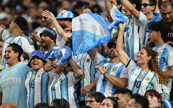 Supporters argentins en tribune, avec un drapeau national, lors d'un match de football.