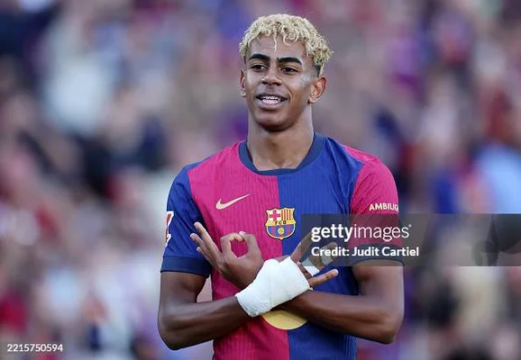 Lamine Yamal souriant et faisant un signe 'OK' sous le maillot du FC Barcelone.