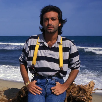 Félix Gray sur une plage, vêtu d'une chemise rayée et de bretelles jaunes.