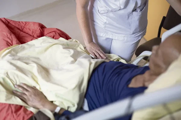 Un soignant auprès d'un patient âgé à l'hôpital, illustrant les soins de fin de vie.