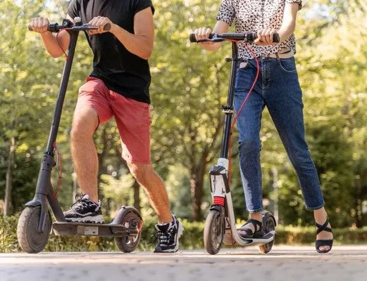 Deux usagers de trottinettes électriques sur une piste dans un parc.