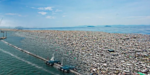 Accumulation massive de déchets plastiques flottant dans le Pacifique, avec un barrage de confinement et des bateaux pour la gestion de la pollution.