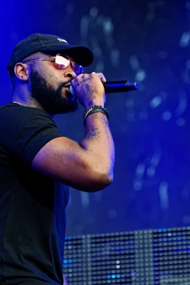 Damso en concert, micro à la bouche, sous une lumière bleue.