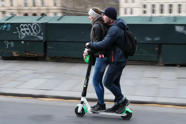 Deux personnes à bord d'une trottinette électrique verte et blanche en ville.