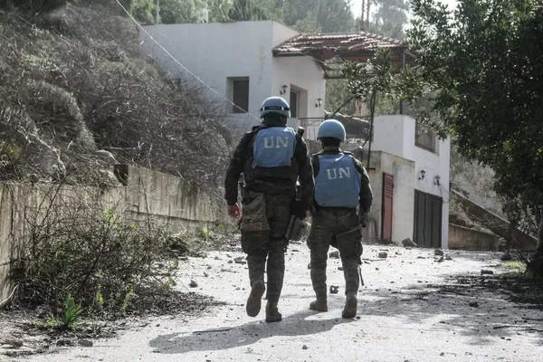 Deux casques bleus de l'ONU marchent dans une rue résidentielle parsemée de décombres.