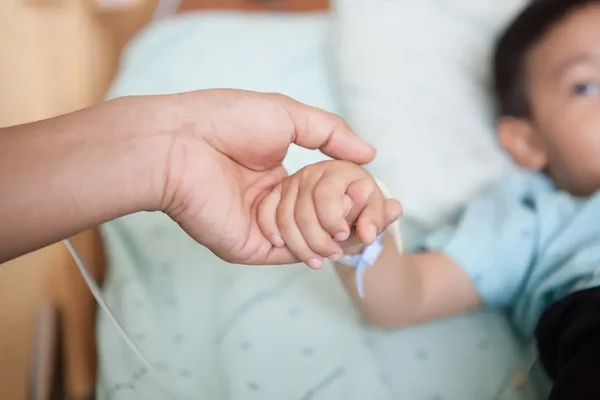 Main d'adulte réconfortant un enfant hospitalisé, avec perfusion et bracelet d'identification.