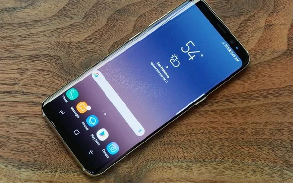Un Samsung Galaxy S8 sur une table en bois, écran allumé avec widget météo et applications, symbole de l'arrêt des mises à jour.