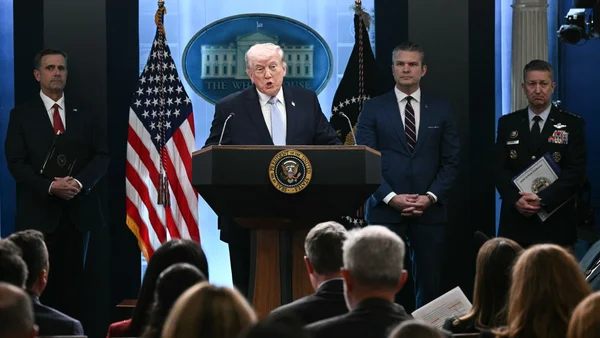 Donald Trump s'adressant à la presse depuis un pupitre présidentiel, entouré de collaborateurs.