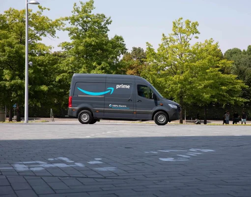 Camionnette de livraison électrique Amazon Prime vue de profil, stationnée sur une surface pavée avec des arbres en arrière-plan.