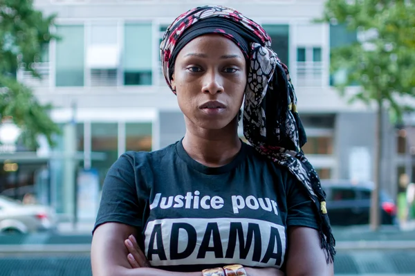 Assa Traoré, bras croisés, en t-shirt 'Justice pour ADAMA' et foulard.