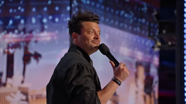 Kev Adams micro en main sur une scène illuminée.