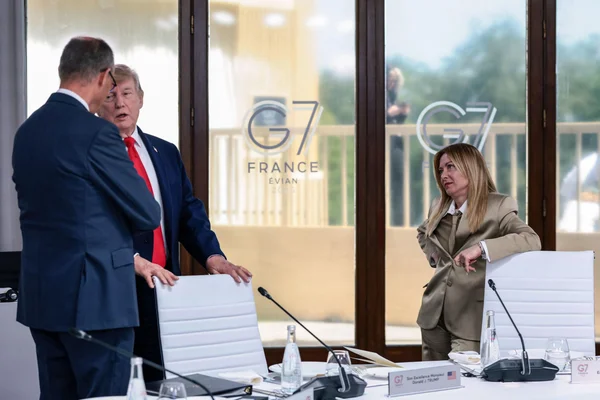 Donald Trump au sommet du G7 à Évian, discutant avec un homme alors qu'une femme en tailleur beige regarde.