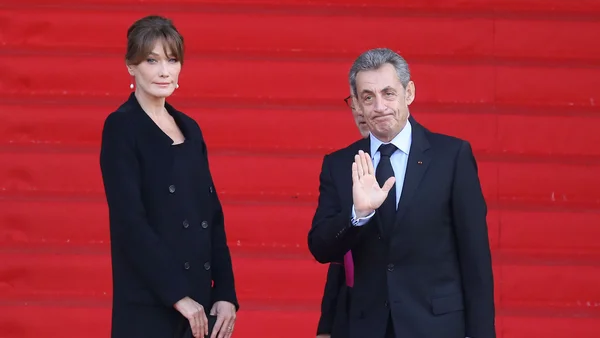 Nicolas Sarkozy et Carla Bruni sur des escaliers rouges, l'ancien président faisant un geste.